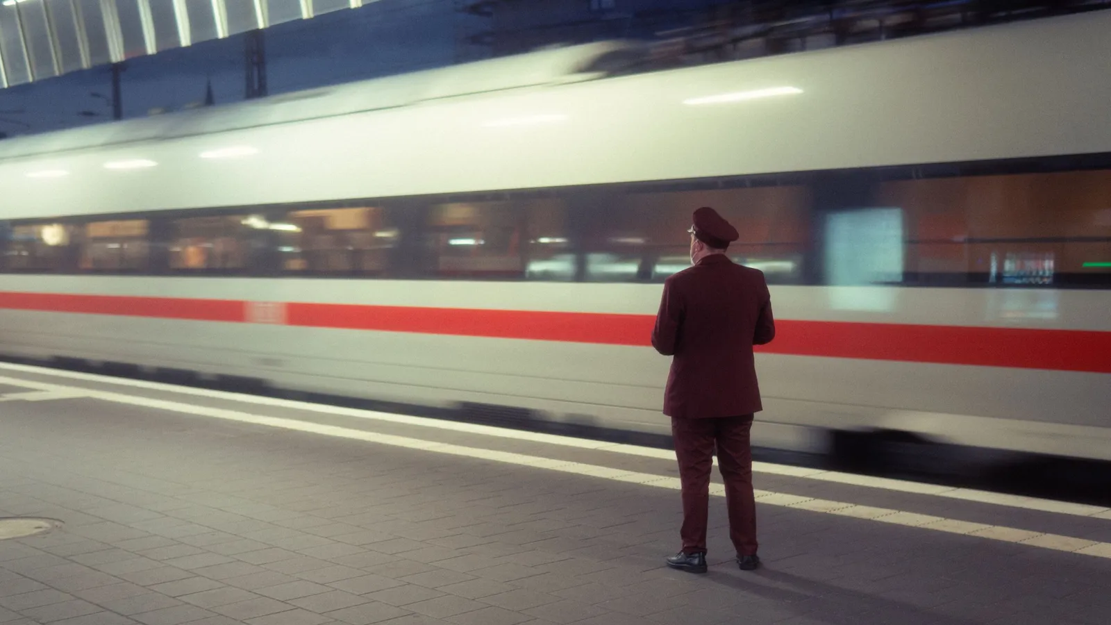 Treinconducteur in uniform kijkt toe terwijl een hogesnelheidstrein bij schemering op een perron aankomt