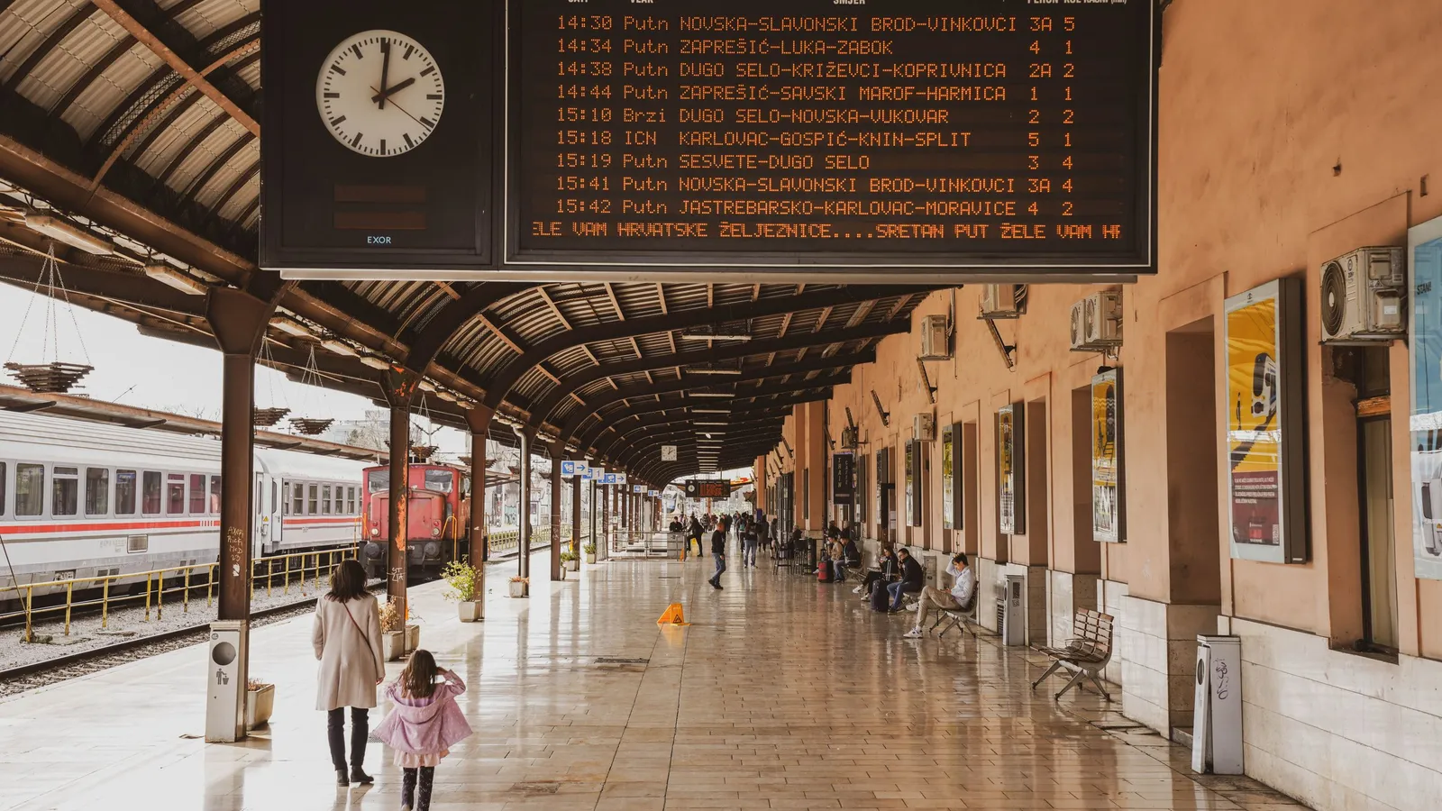 Vertrekbord met klapcijfers waarop treintijden op een Kroatisch station staan, met een klok erboven