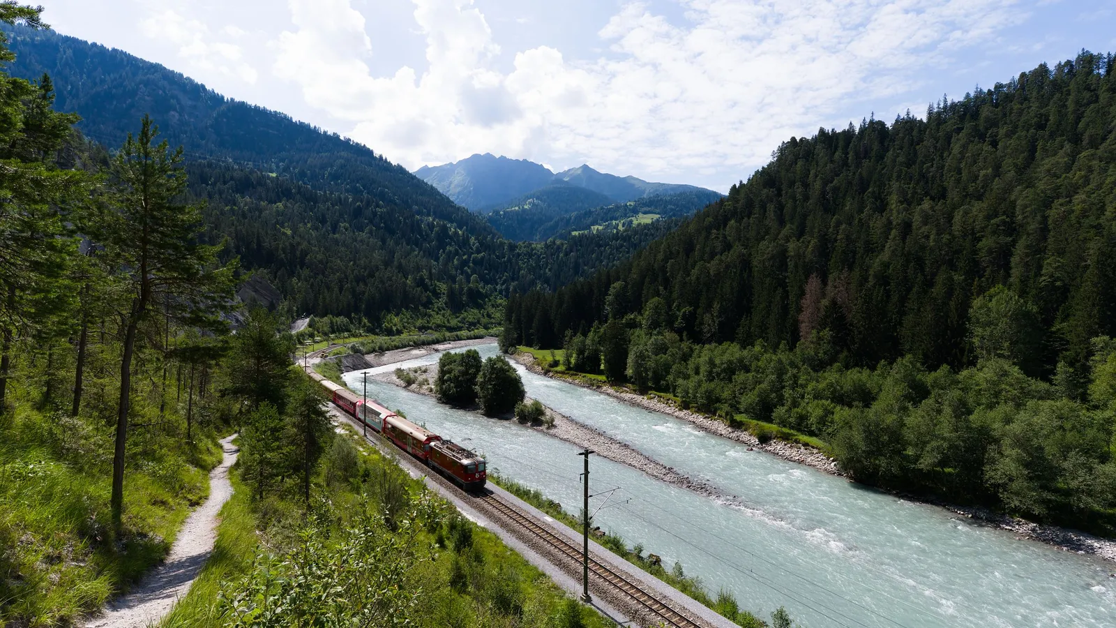 Een rode trein van de Rhätische Bahn volgt een turkooizen rivier door een bebost Zwitsers alpendal