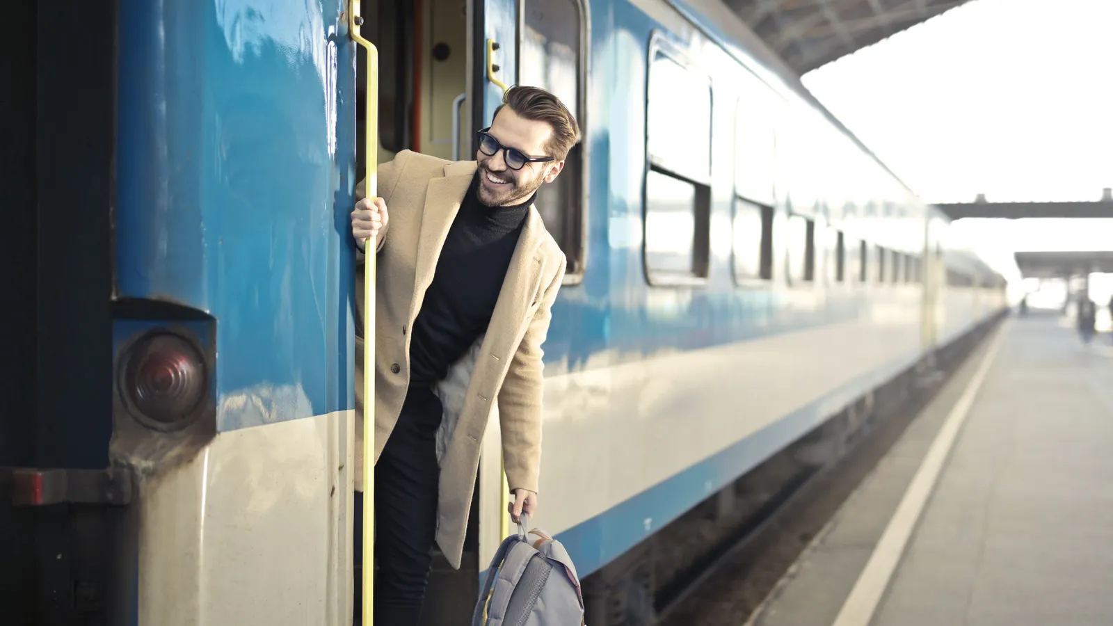 Jonge man met een rugzak die op een trein stapt op een Europees stationsperron