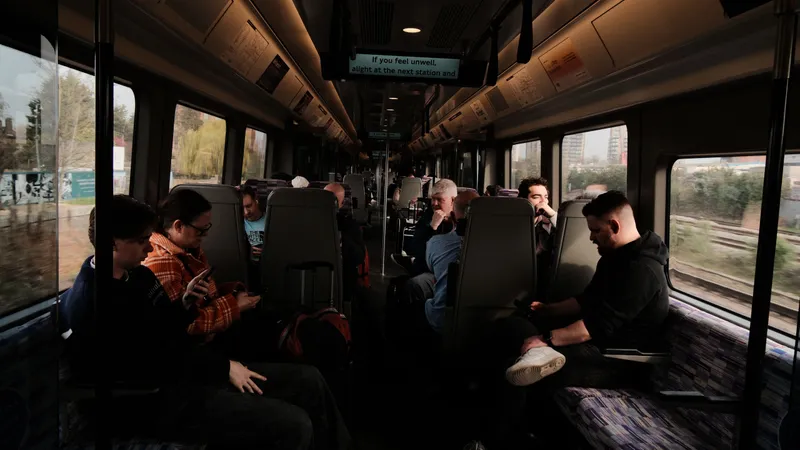 Passengers seated in a train carriage, one checking a phone, countryside blurring past the windows