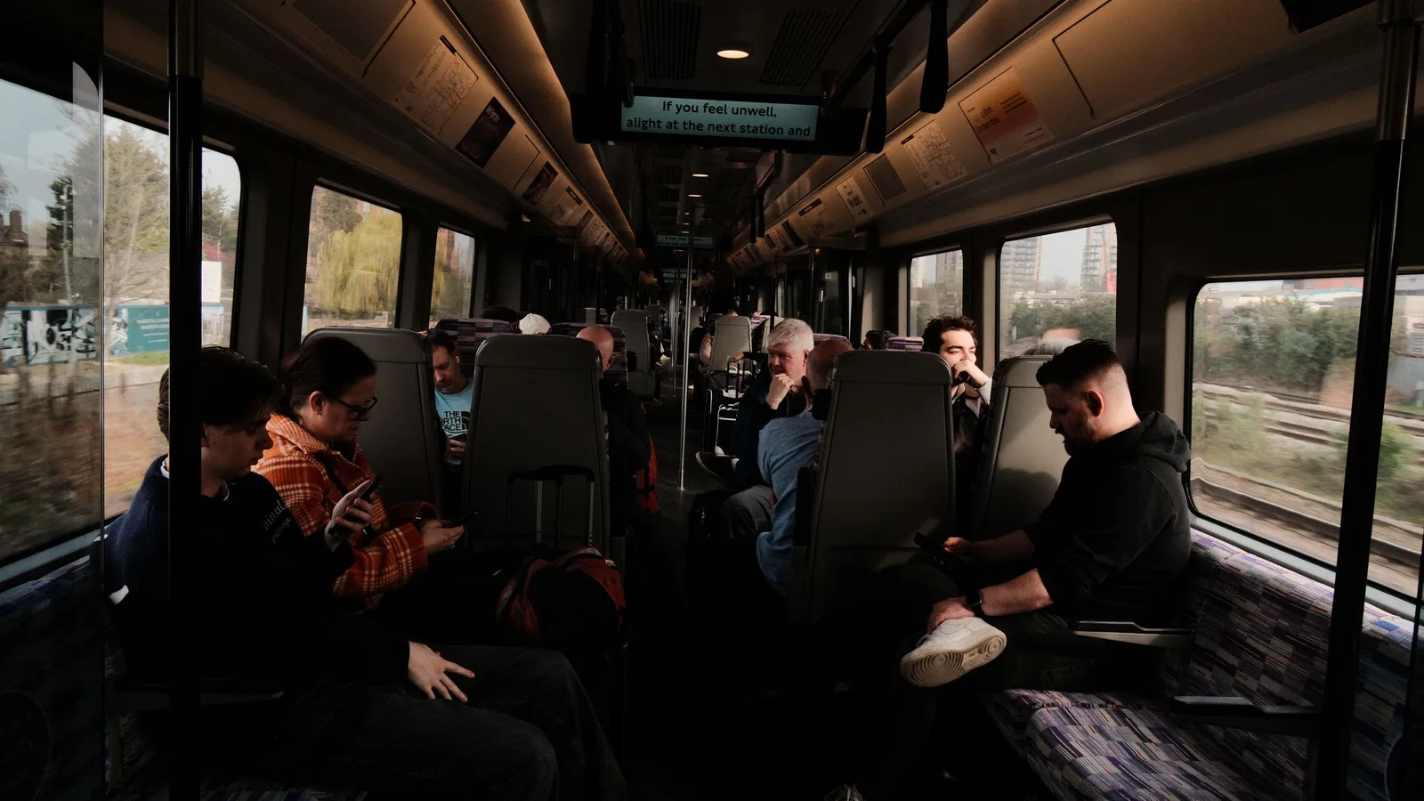 Passagiers in een treinwagon, van wie één op een telefoon kijkt terwijl het landschap buiten de ramen vervaagt