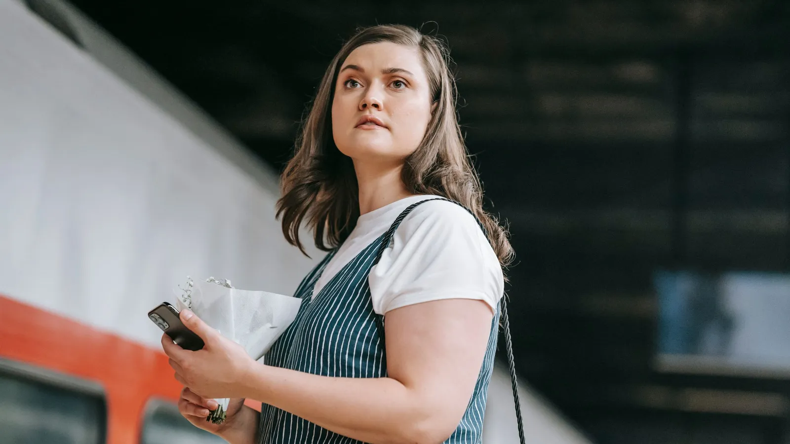 Een vrouw houdt haar telefoon vast op een perron naast een treinrijtuig
