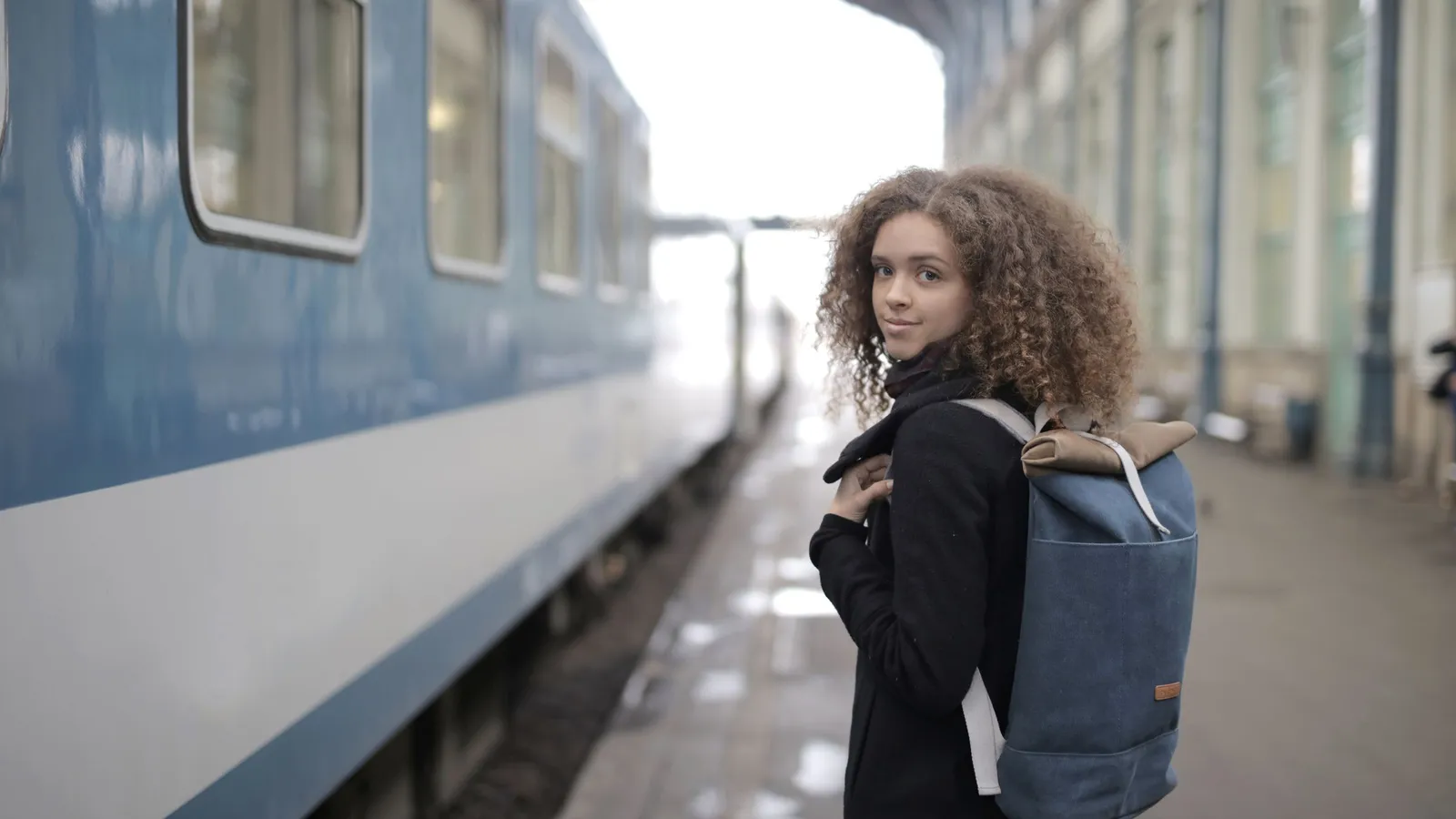 Jonge vrouw met een rugzak staat op een perron naast een rijtuig