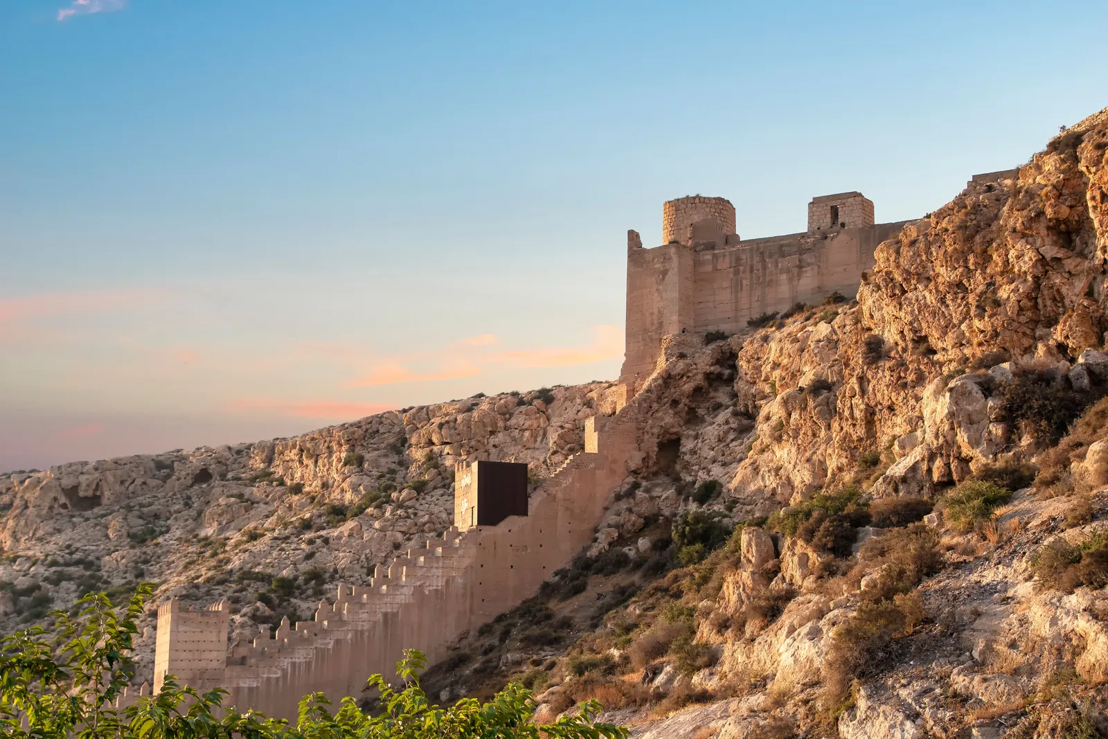 Mura e torri della fortezza dell'Alcazaba che salgono sul pendio roccioso sopra Almería nella calda luce della sera