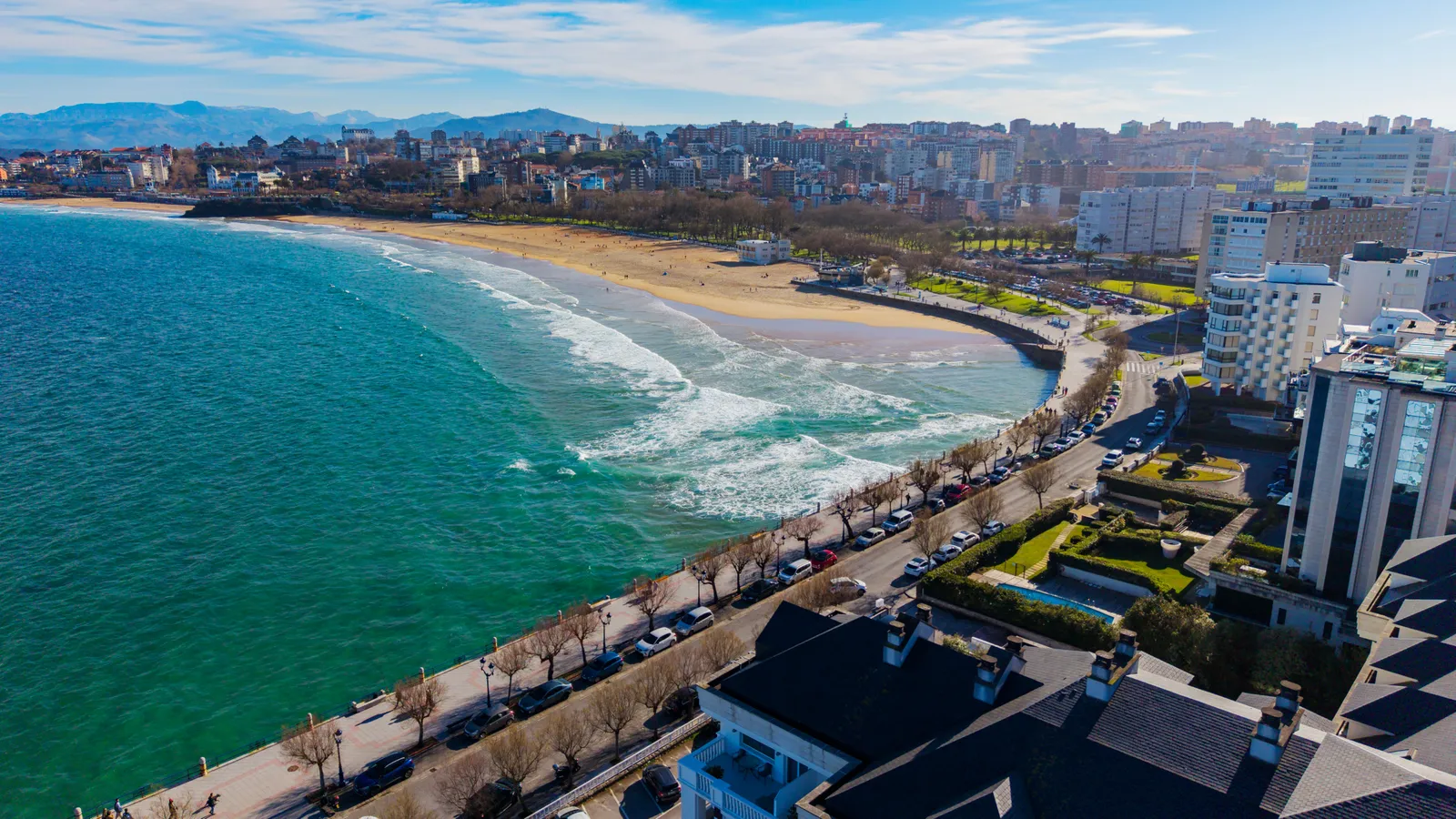 Aerial view of El Sardinero beach and its seafront promenade in Santander, with the city and mountains behind