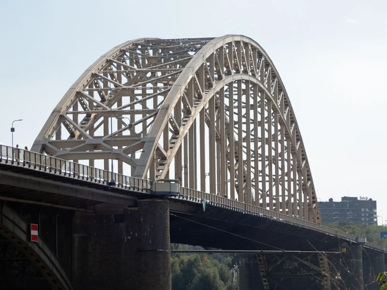 The steel arch of the Waalbrug road bridge over the Waal in Nijmegen, seen from the riverbank under a clear sky