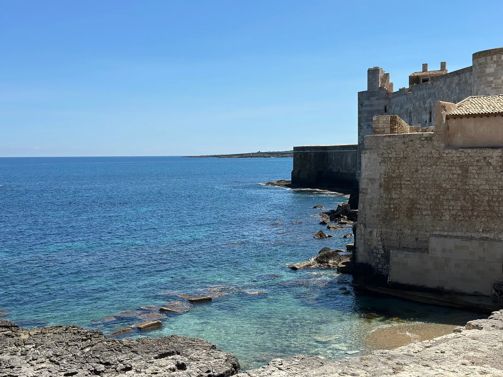 Befästningsmurar av sten och klarblått hav vid kusten på ön Ortigia i Syrakusa, Sicilien