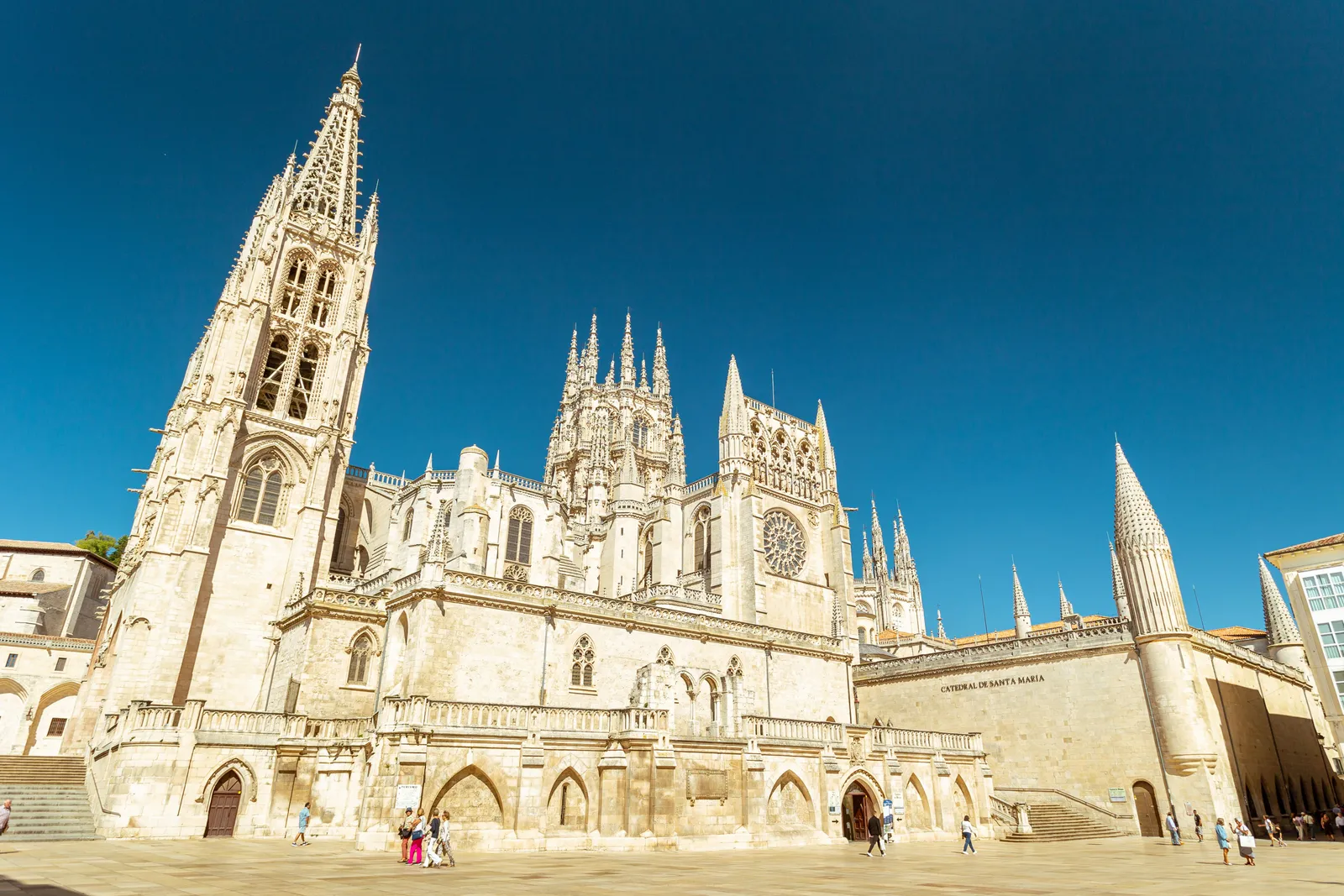 Le guglie gotiche e la facciata sud della cattedrale di Burgos in piena luce, con pochi visitatori sulla piazza di pietra
