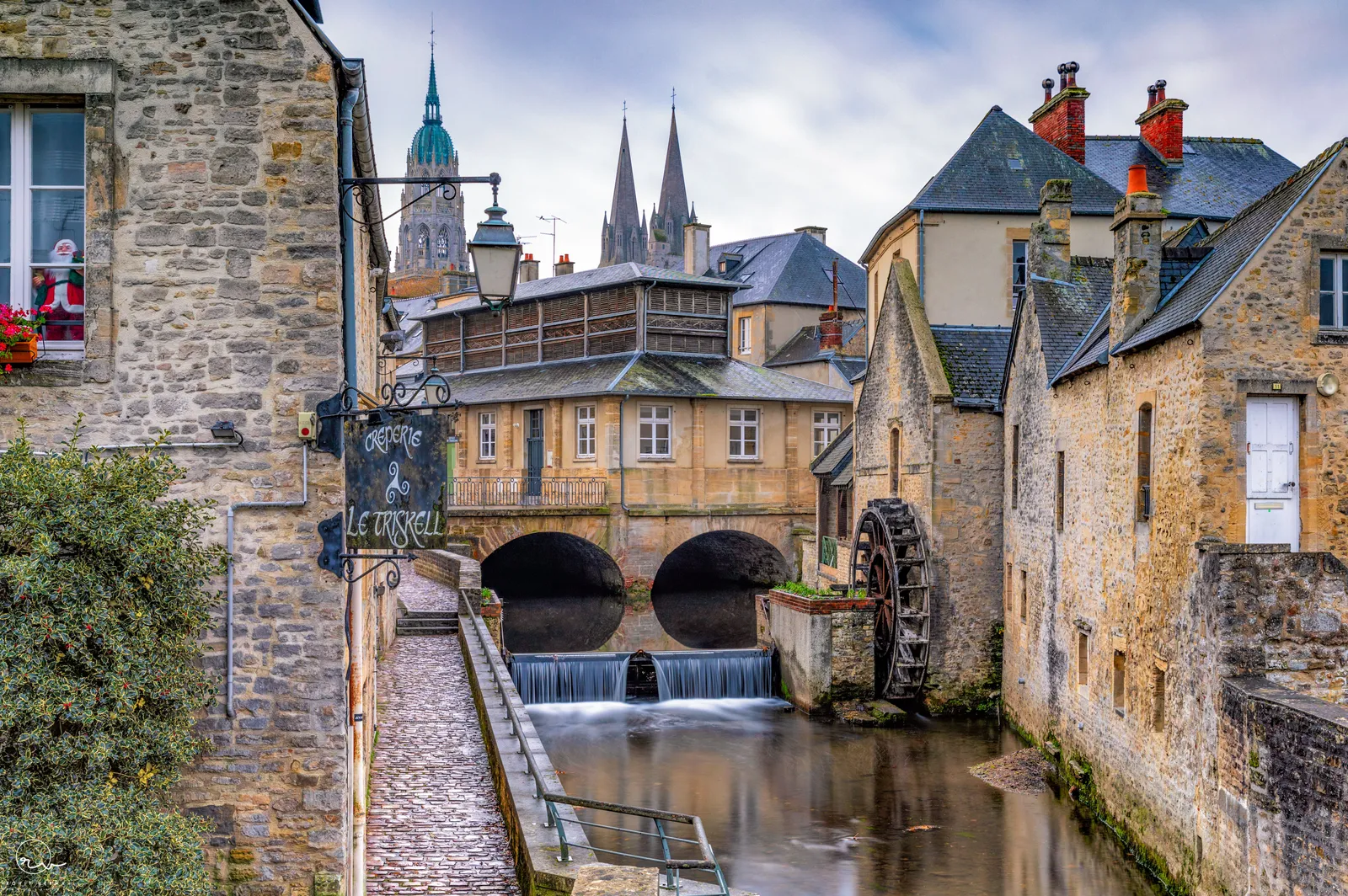 Old watermill on the Aure in Bayeux with the cathedral spires rising behind the stone houses